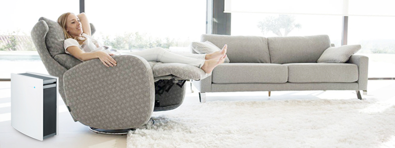seorang wanita yang sedang bersantai di sofa dan menggunakan air purifier di rumahnya untuk membersihkan udara