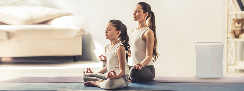 Ibu dan Anak sedang melakukan yoga di rumah dan menggunakan air purifier untuk menetralisir udara